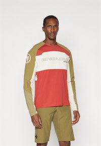Maglia a maniche lunghe con sezioni rosse, bianche e olive, dotata di dettagli di ventilazione. Abbinate a pantaloni corti olive. Logo sulla maglia e sui pantaloni.