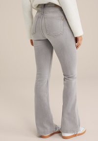 Graue, aus Denim gefertigte, weit ausgestellte Jeans mit hoher Taille, ausgestattet mit zwei Gesäßtaschen und hellen Nähten. Kombiniert mit weißen Sneakers und einem gestrickten Pullover.