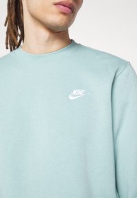 Sudadera azul claro de tejido suave, con cuello redondo y un pequeño logo de Nike en blanco bordado en el pecho.