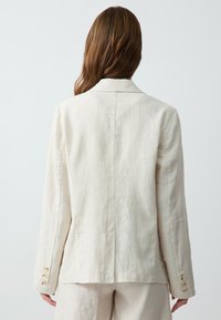 Leinenblazer in hellbeige mit tailliertem Schnitt, Reverskragen und vierknöpfigemverschluss an den Ärmeln. Glatte Textur und minimalistisches Design.
