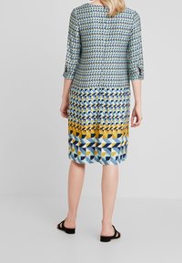 Vestido multicolorido con patrones geométricos en azul, amarillo y negro. Mangas tres cuartos y diseño a la altura de la rodilla con un ajuste relajado.