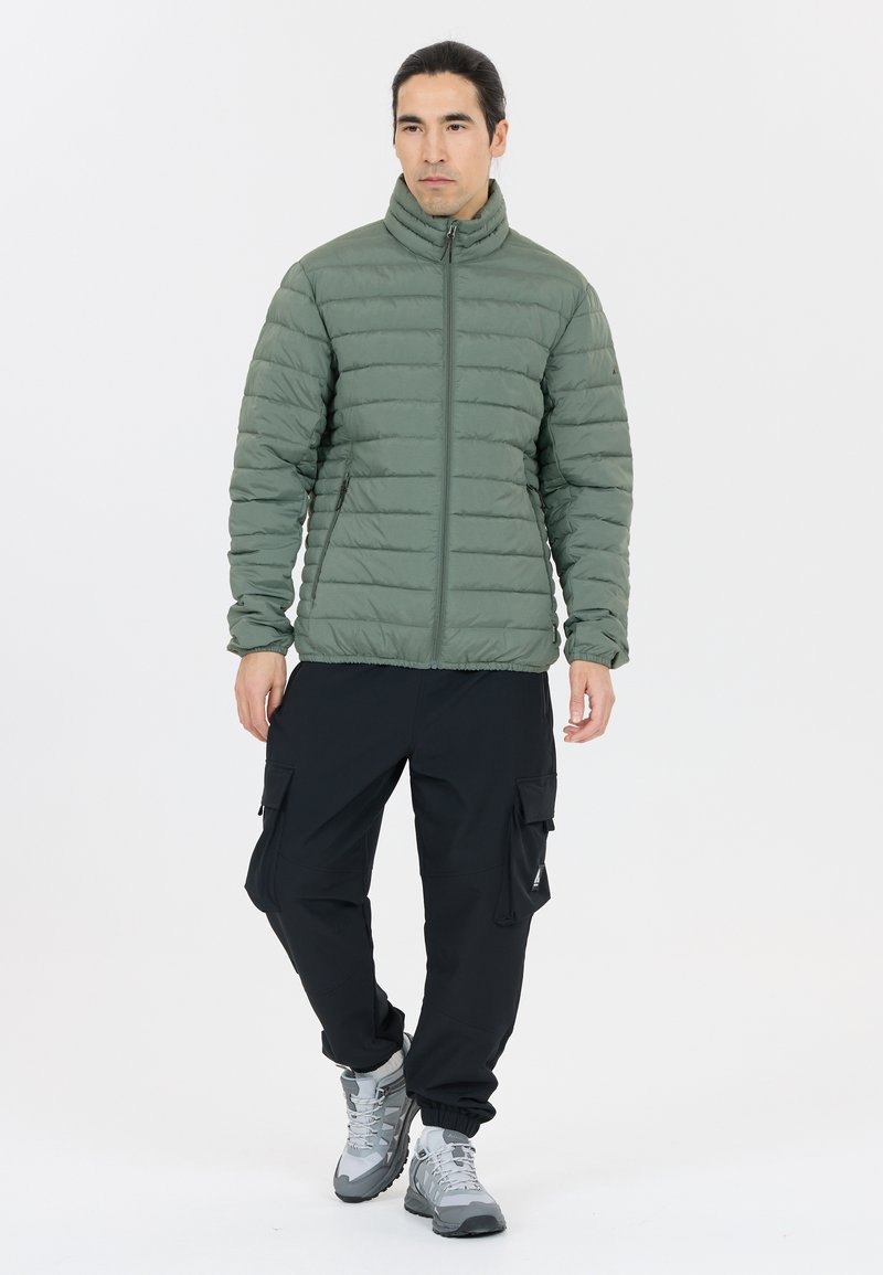 Grüne Puffjacke mit Stehkragen und horizontaler Steppung. Kombiniert mit schwarzen Cargo-Hosen und grauen Wanderschuhen.