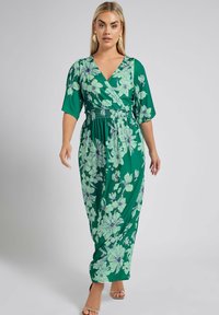 Vihreä kukkakuviollinen mekko, joka on valmistettu kevyestä kankaasta. Siinä on lyhyet hihat ja kapea vyötärö, jossa on suuria vaaleansinisiä kukkakuviota.