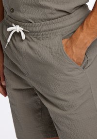 Grå texturerade shorts med resårmidja, utrustade med en vit dragsko och sidofickor. Tyget har ett subtilt mönster och en mjuk finish.
