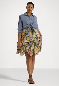 Camicia button-up a righe blu legata in vita; gonna a rouches con motivo floreale in tessuto leggero con dettagli rosa, blu e gialli. Sandali con cinturini.