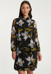 Blumenkleid aus einem schwarzen, durchsichtigen Stoff, mit langen Puffärmeln, einem rüschigen Kragen und bunten Blumenmustern in Rosa- und Blautönen.