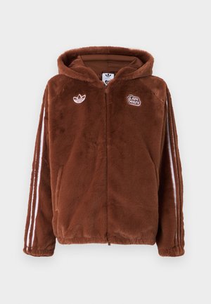 Homme portant un sweat à capuche en peluche marron avec des oreilles d'ours sur la capuche et un ours tenant un cœur rouge cousu dans le dos, associé à un jean bleu.