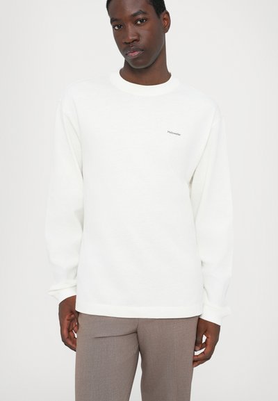 White sweatshirt with long sleeves, round neckline, and soft texture. Features subtle "Halzweiler" logo on the chest and relaxed fit.
