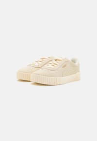 Sneaker beige in suede con suola piatta testurizzata, dotate di lacci tonali e un branding sottile sui lati e sulla linguetta. Interno liscio.