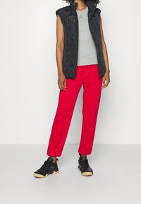 Black quilted vest with a high collar, gray fitted t-shirt, and loose red pants. Black sneakers with beige soles complete the look.