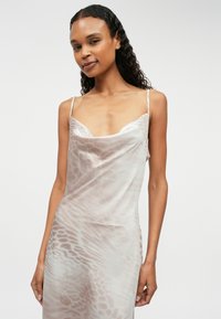 Σατέν φόρεμα σε ήπιο μπεζ χρώμα με διακριτικό ζώο σχέδιο, που διαθέτει λεπτές τιράντες και χαλαρή, ρέουσα σιλουέτα.