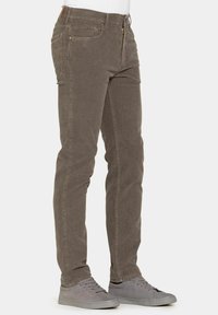 Pantaloni in corduroy marrone con un design slim fit, dotati di una zip frontale, cinque tasche e dettagli di cucitura sottili. Abbinati a sneaker grigie.