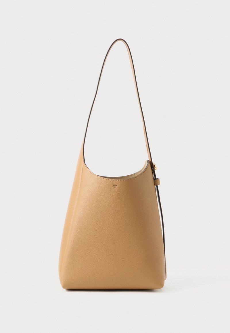 Sac en cuir léger couleur beige clair, avec une texture lisse, un design minimaliste, une seule sangle incurvée et des détails matériels discrets.