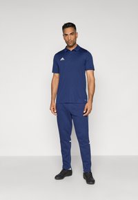 Polo de color azul marino con mangas cortas y cuello, combinado con pantalones de chándal a juego que tienen rayas laterales blancas y zapatillas deportivas negras.