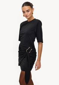 Robe noire froncée en tissu doux, avec ceinture ornée d'une boucle dorée et manches courtes. Texture lisse et coupe ajustée.