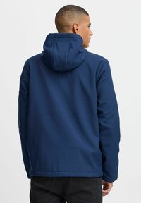 Veste à capuche bleu marine avec une finition lisse et mate, dotée d'une capuche à cordon de serrage et d'une coupe simple, portée sur un pantalon noir.