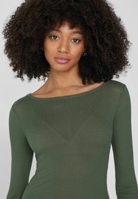 Ripp-Shirt mit langen Ärmeln in Dunkelgrün, ausgestattet mit einem weiten Bootsausschnitt und einer taillierten Silhouette. Weicher Stoff, leichtes Material.