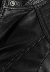 Crna kožna tkanina koja sadrži glatka i teksturirana područja, s vidljivim šavovima i detaljem na dugmetu za zatvaranje. Prisutni su geometrijski kviltani uzorci.