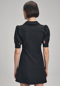 Abito nero con colletto, maniche a sbuffo e polsini abbottonati. Corpino aderente che porta a una gonna a campana. Tessuto morbido al tatto.