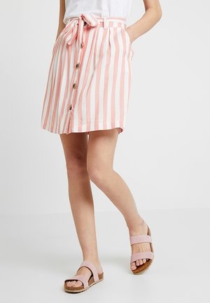 Różowo-biała spódnica w paski z bawełny z wiązaniem w talii, guzikami z przodu i bocznymi kieszeniami, zestawiona z jasnoróżowymi klapkami na płaskiej podeszwie.