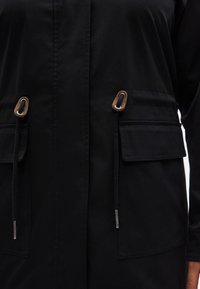 Μαύρο μπουφάν με διπλές μπροστινές τσέπες, κλείσιμο με κορδόνια και μεταλλικές λεπτομέρειες. Λείο ύφασμα και ραμμένη σχεδίαση για εφαρμοστή εμφάνιση.