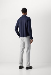 Camicia blu navy con colletto classico, maniche lunghe e una texture liscia, abbinata a pantaloni grigi chiari e scarpe nere.