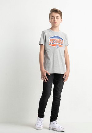 Camiseta de algodón gris con un gráfico en naranja y azul que dice "PETROL", combinada con jeans slim-fit negros y zapatillas blancas.
