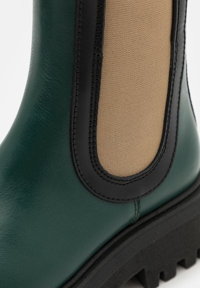 Bota de tornozelo verde em pele com acabamentos em preto e um painel elástico em castanho, com uma sola de borracha texturizada e um design robusto e chunky.