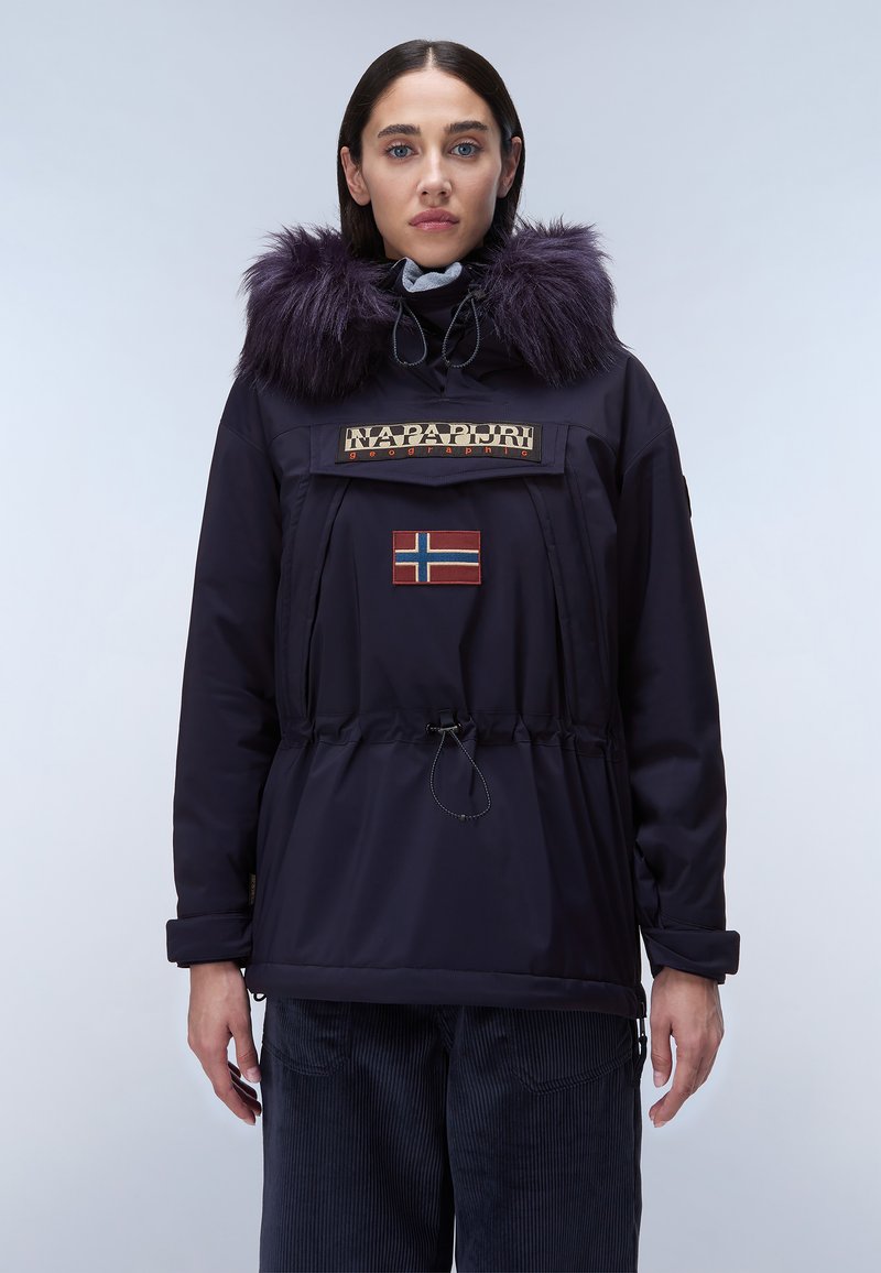 Mörkblå parkajacka med fuskpäls på huva, dragsko i midjan, framfickor med dragkedja och broderad norsk flagga. Elastiska ärmslut och slitstukt tyg.