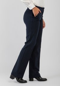 Pantaloni navy a righe con una vestibilità su misura, caratterizzati da una texture liscia, chiusura con bottone e tasche laterali, abbinati a stivali neri con tacco.