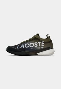 Lacoste atletska obuća u tamnozelenoj i crnoj boji s bijelim logotipom. Ima glatki sintetički materijal, teksturirane vezice i pjenasti potplat.
