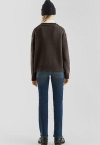 Donkerbruine gebreide trui met een geribde zoom, gedragen met blauwe jeans. De persoon draagt ook een zwarte gebreide beanie. Het achteraanzicht toont de outfit.