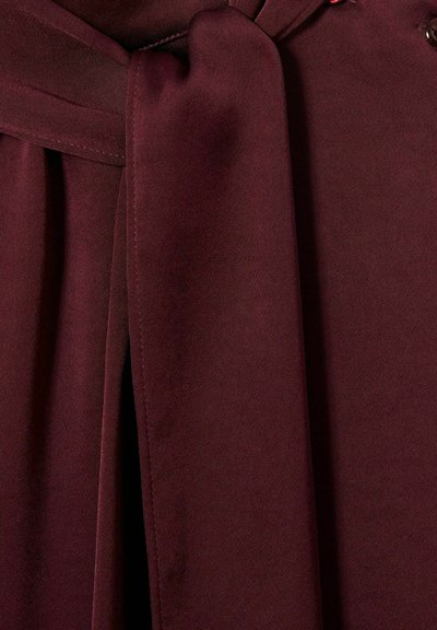 Tessuto bordeaux dalla texture morbida, con cintura annodata e cuciture rifinite con cura. Il design mette in risalto il drappeggio e la fluidità.