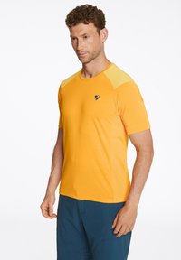 Camiseta atlética de manga corta en color naranja, fabricada con un material ligero y detalles de malla en los hombros. Presenta un pequeño logotipo en el pecho.