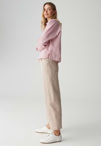 Pasekowana różowo-biała koszula na guziki, luźny krój, zestawiona z beżowymi spodniami o szerokich nogawkach i białymi tenisówkami. Gładka tkanina, boczne rozcięcia.