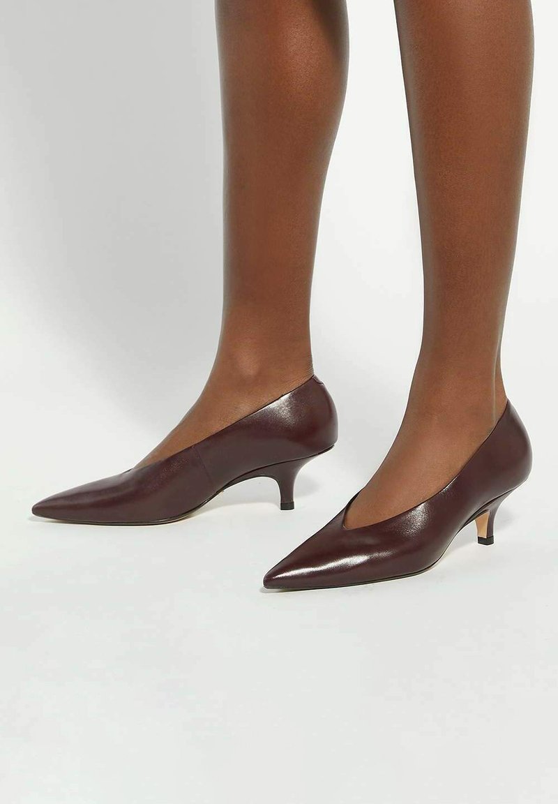 Burgundy leather kitten heels with a pointed toe, slightly shiny texture, and a low cone heel. Sleek design with a v-cut sides.