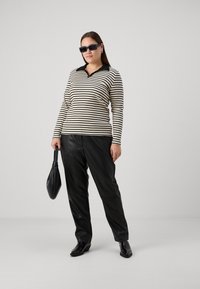 Camisa polo de manga larga a rayas en crema y negro, combinada con pantalones de piel sintética negros. El modelo sostiene un bolso negro y lleva gafas de sol oscuras.