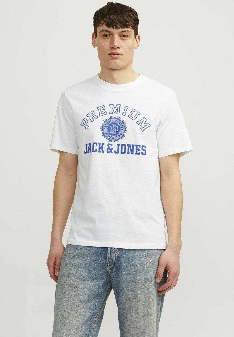Valkoinen puuvillainen T-paita, jossa on sininen tulostettu teksti "PREMIUM JACK & JONES." Ominaisuuksiin kuuluu pyöreä kaula-aukko ja lyhyet hihat, yhdistettynä vaaleansinihin farkkuihin.