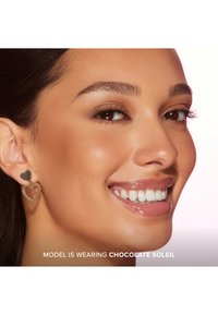 Gouden hartvormige oorbellen hebben een kleine solide hart aan de bovenkant en een open hartontwerp daaronder. Het model heeft een zachte huid en een stralende glimlach.