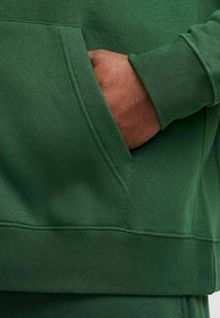 Grön bomullströja med framficka, ribbad mudd och fåll, med en mjuk textur och rena sömmar.