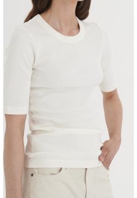 Vit ribbad stickad topp med kort ärm och rund halsringning. Tyget har ett strukturerat mönster och en figurnära passform.