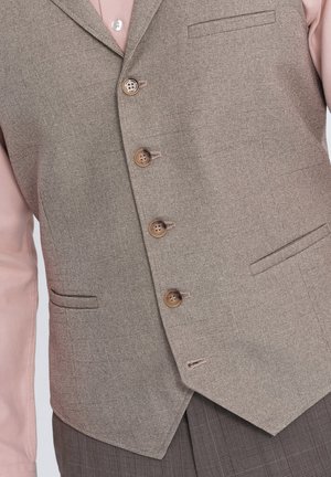 Chaleco marrón claro hecho de tejido texturizado, con seis botones, dos bolsillos frontales y un cuello con muesca. Lleva encima una camisa rosa.