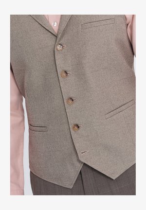 Hellbraune Weste aus strukturiertem Stoff mit sechs Knöpfen, zwei Fronttaschen und einem aufgeschlagenen Kragen. Getragen über einem pinken Hemd.