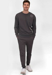 Sweat-shirt gris avec un col rond et un logo sur la poitrine, associé à un pantalon fuselé assorti. Le tissu semble doux, avec des poignets élastiques.