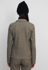 Grå rutigt kavaj med skräddarsydd passform, tillverkad av texturerad tyg. Kombineras med en svart stickad mössa, vilket ger en enkel och avslappnad look.