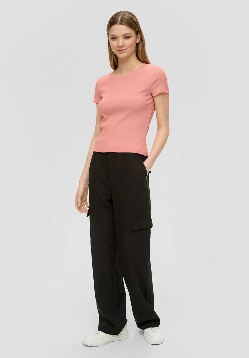Roze ribbeltop met korte mouwen, gecombineerd met zwarte cargobroek met zakken, gedragen met witte sneakers. Eenvoudig ontwerp en casual pasvorm.