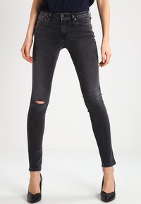 Jeans ajustados negros con un acabado desgastado, que presentan un detalle de rodilla rasgada, diseño de cinco bolsillos y una cintura de altura media.