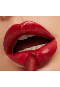 Red lipstick applied to full lips, showcasing a glossy finish and smooth texture. The lipstick tube is partially visible in the mouth.