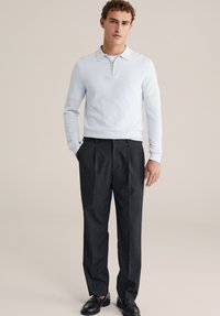 Svetlo modra polo majica z dolgimi rokavi in zadrgo na ovratniku, kombinirana s temno sivimi hlačami z naborki in črnimi elegantnimi čevlji. Preprost dizajn in krojen kroj.