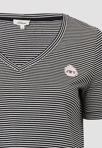 Gestreiftes V-Ausschnitt-T-Shirt in Schwarz und Weiß, mit horizontalen Streifen und einem rosa "JOY"-Logo-Patch in der Nähe des Halsausschnitts. Weiches Baumwollmaterial.